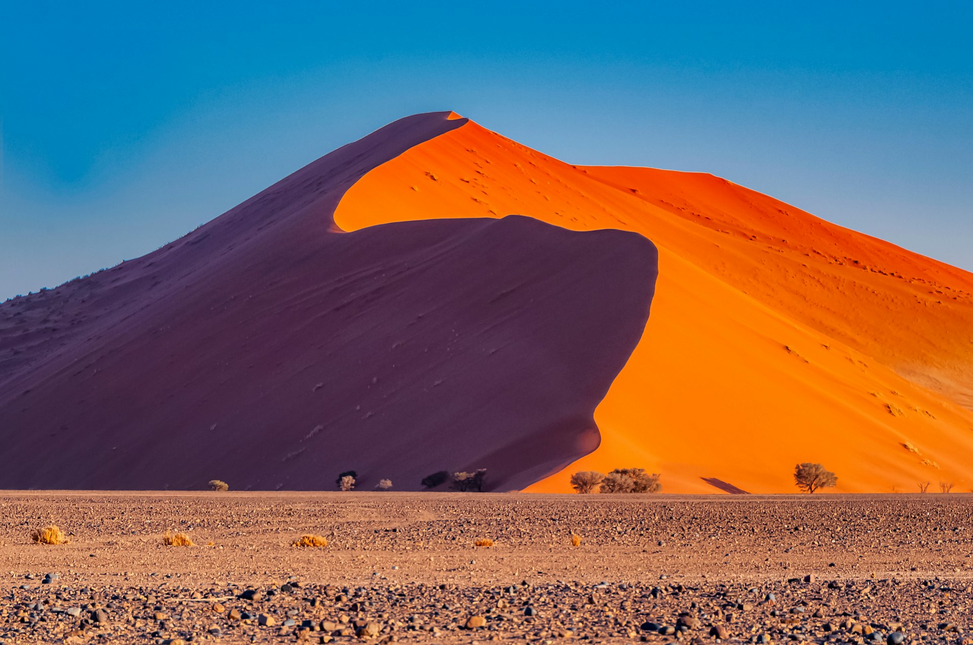 Des dunes de sable rouges du désert de Sossusvlei sous un ciel bleu en journée.