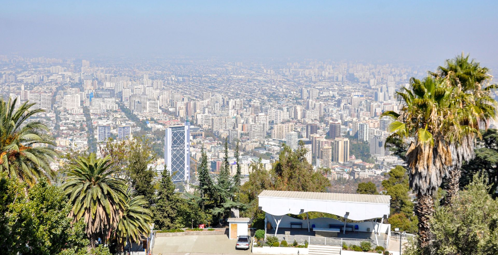 Vue panoramique de Santiago du Chili depuis le Cerro San Cristóbal, avec la silhouette de la ville et les palmiers.