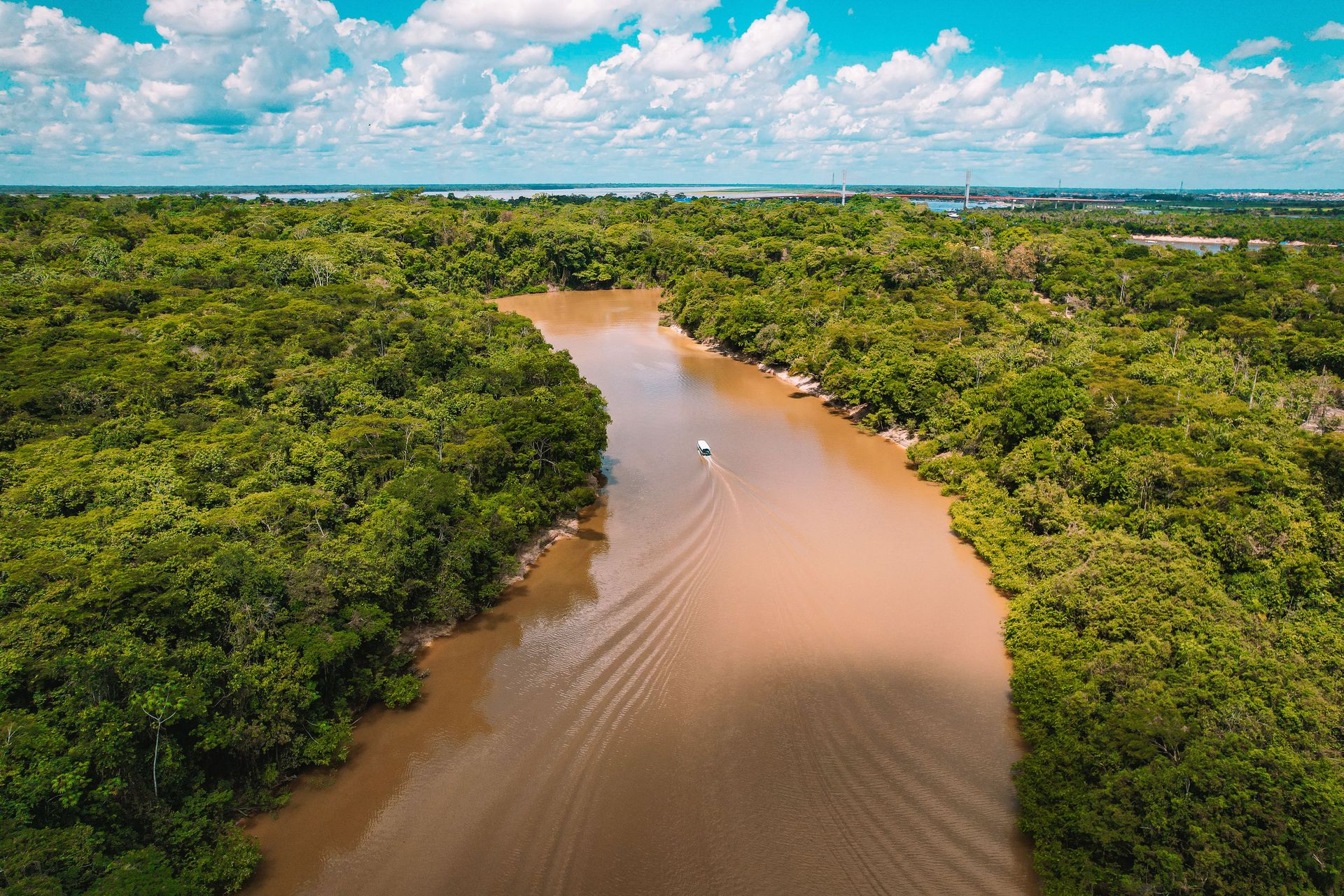 Une prise de vue aérienne pittoresque d'un bateau naviguant sur la rivière amazonienne boueuse entourée d'une forêt tropicale luxuriante.