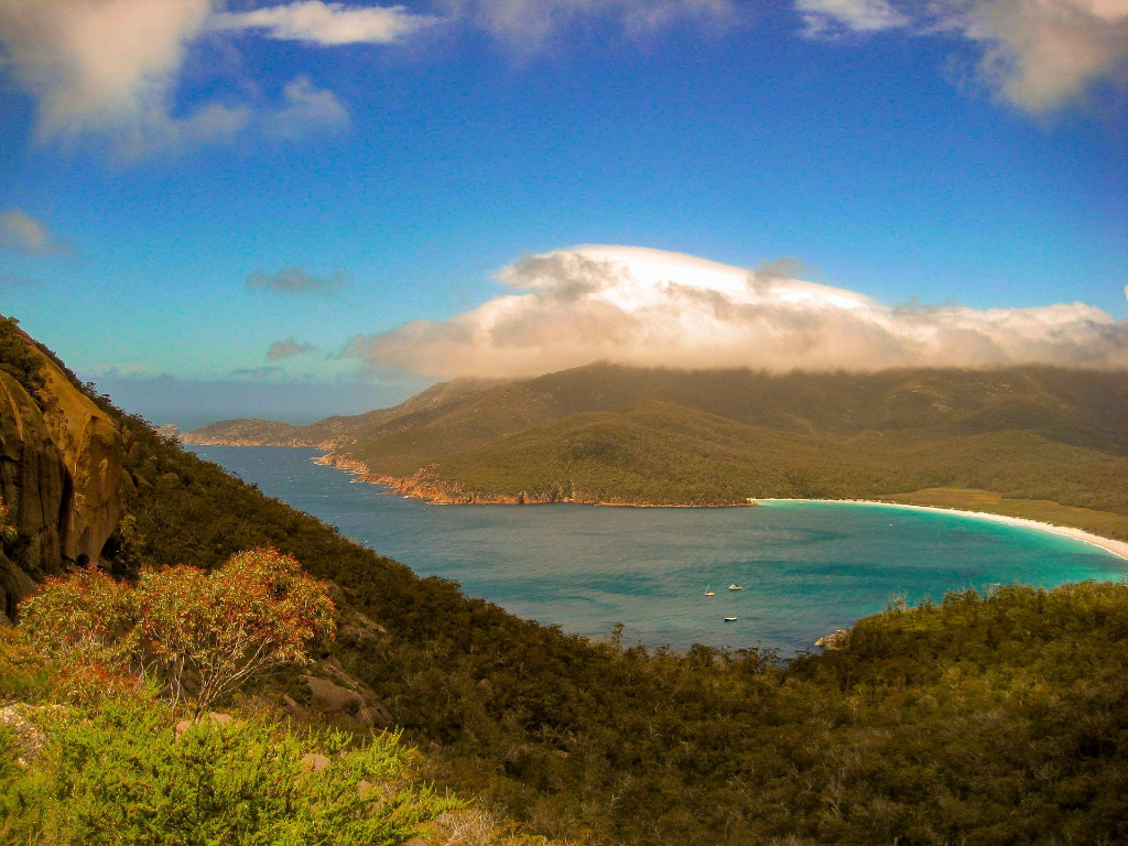 Magnifique vue aérienne de Wineglass Bay avec des eaux cristallines et une végétation luxuriante sous un ciel ensoleillé.