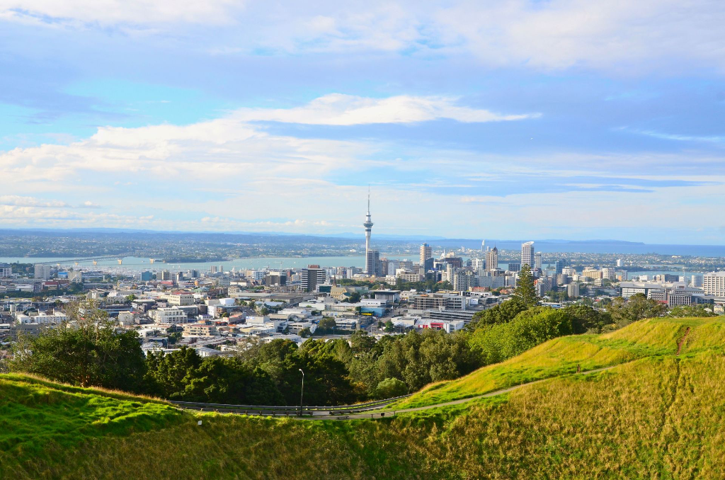Vue imprenable sur le paysage urbain d'Auckland avec la Sky Tower et les collines luxuriantes sous un ciel clair.
