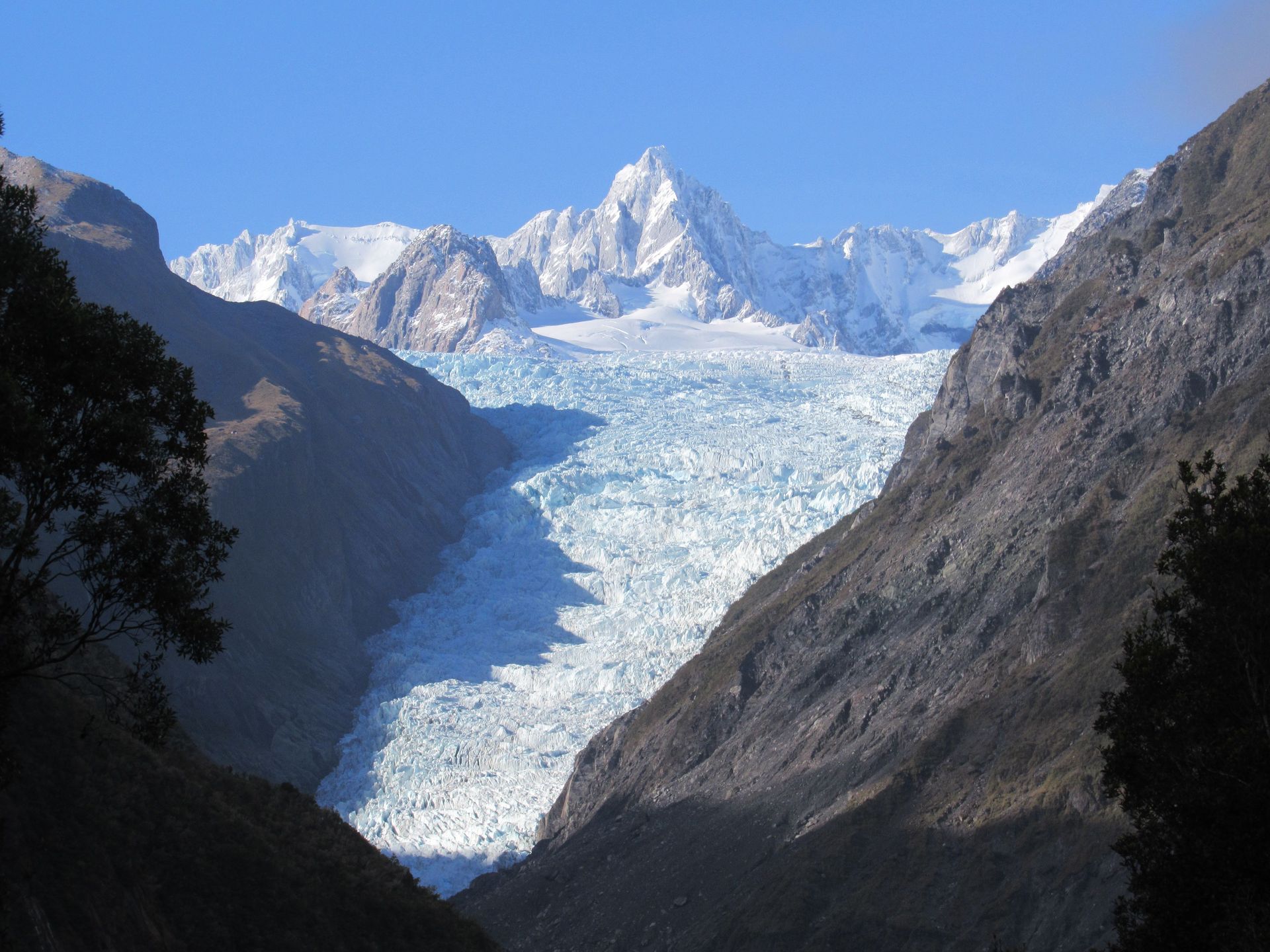 Vue à couper le souffle d'un glacier enneigé entouré de montagnes escarpées sous un ciel bleu.