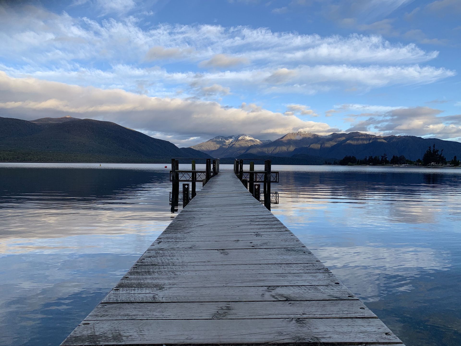Promenade paisible menant à un lac serein dans le Southland, avec un arrière-plan montagneux.