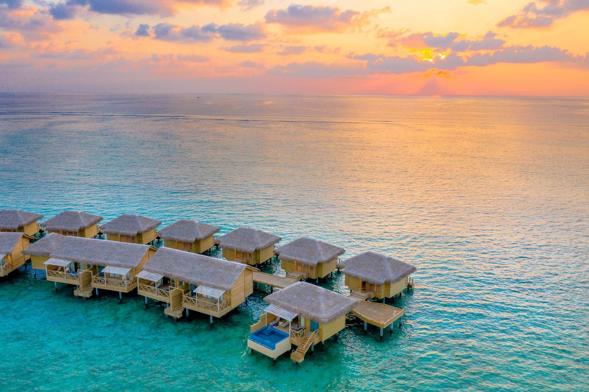 Vue aérienne de magnifiques villas sur l'eau avec un coucher de soleil vibrant sur un océan tropical.