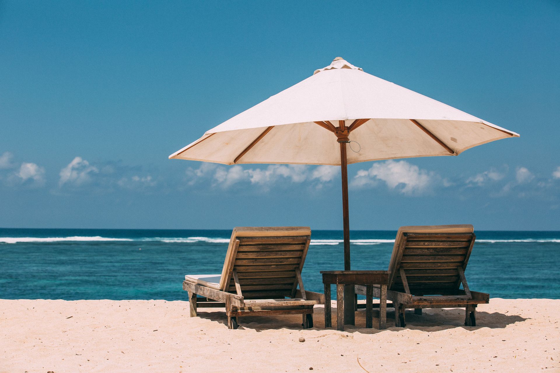 Deux chaises longues sous un parasol sur une plage de sable tranquille avec un ciel bleu.