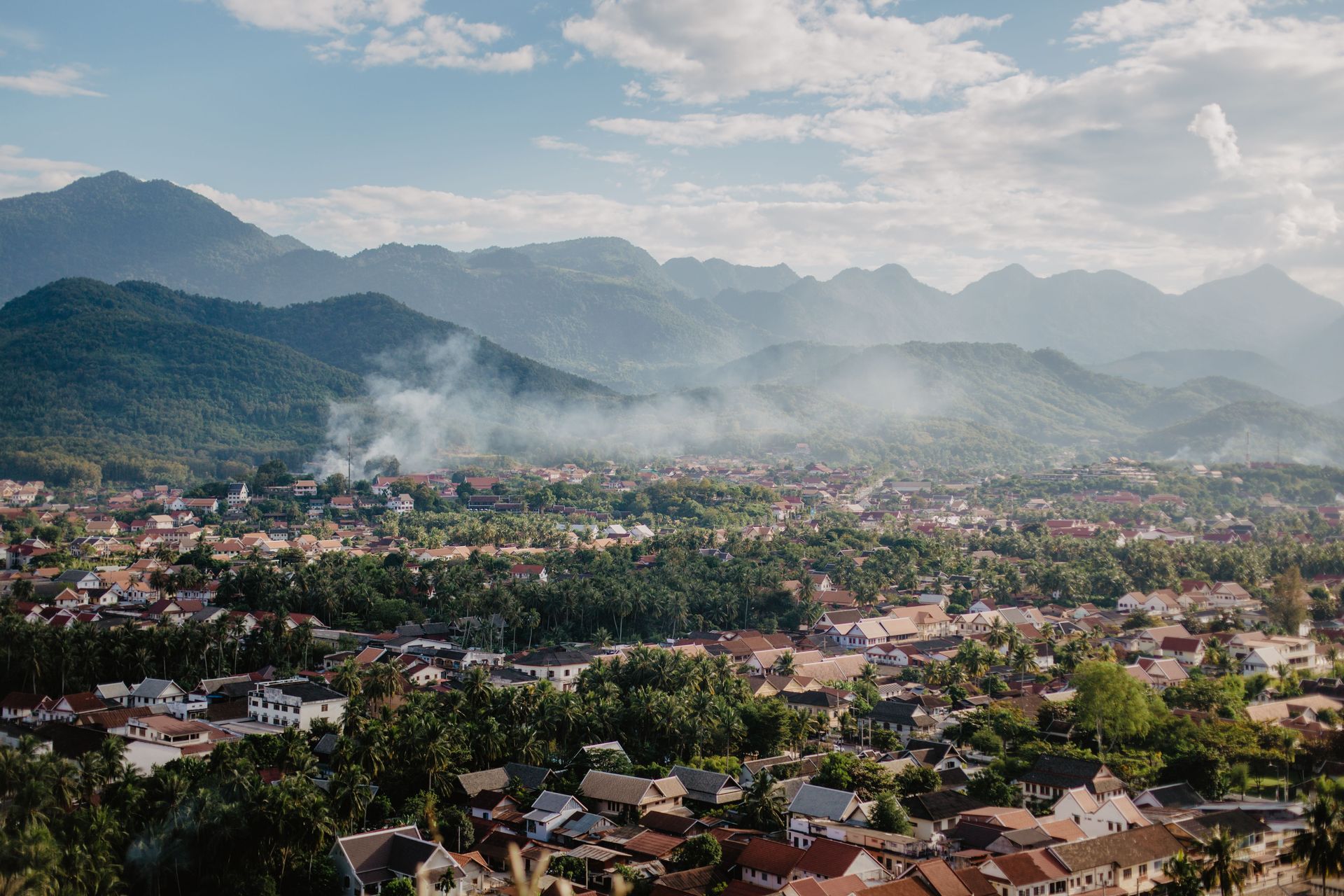 Vue aérienne à couper le souffle d'un village niché parmi des montagnes verdoyantes sous un ciel lumineux.