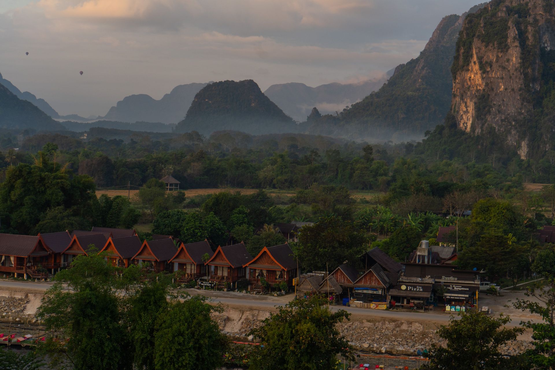 Vue de paysage apaisante de Vang Vieng, Laos, mettant en valeur des huttes, des montagnes et un paysage brumeux.
