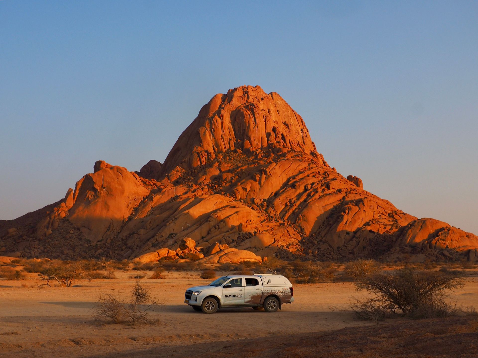 Coucher de soleil spectaculaire sur Spitzkoppe dans la région de Damaraland, en Namibie, avec une voiture au premier plan.