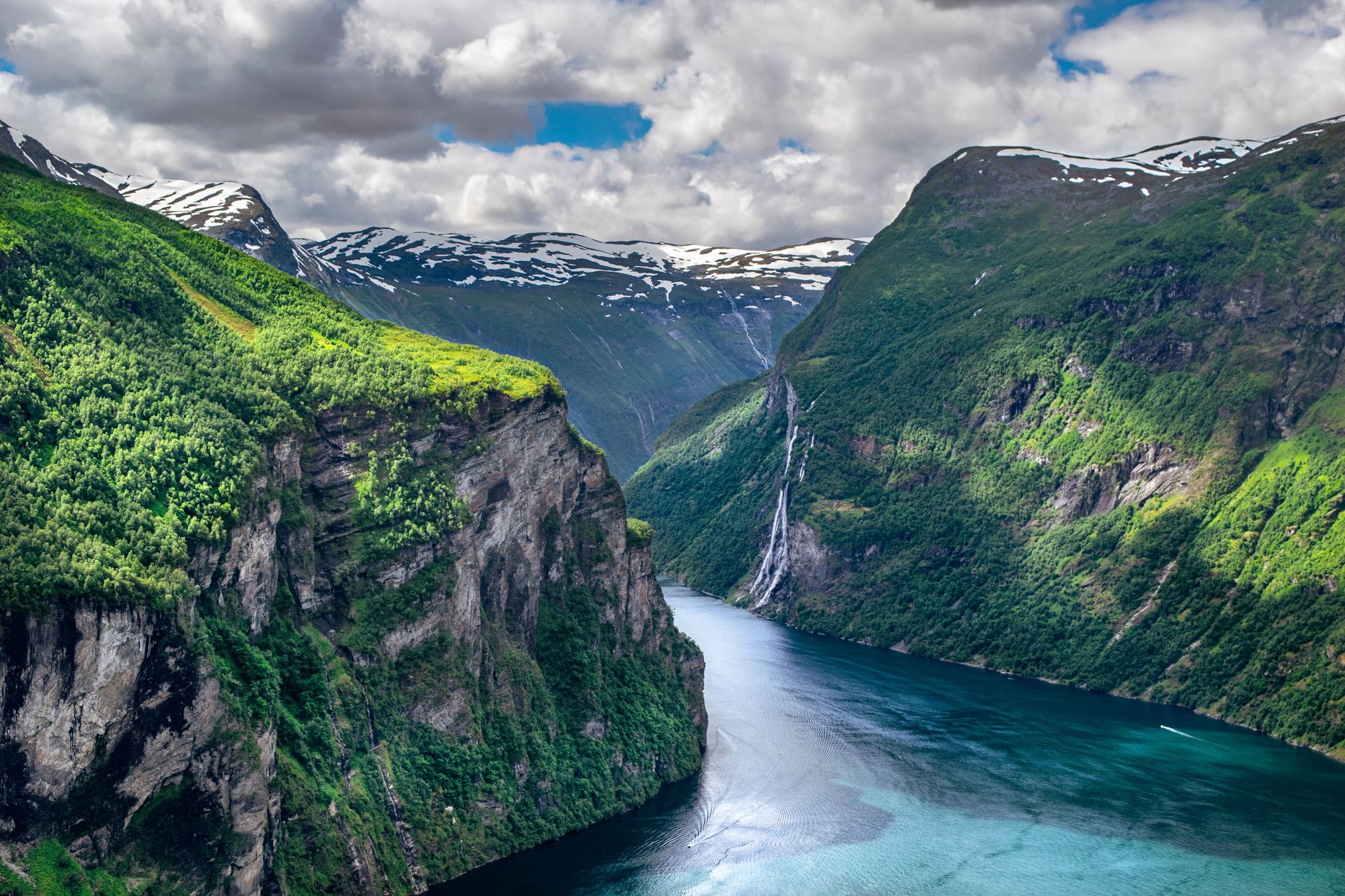 Vue magnifique d'un fjord de Norvège avec des montagnes luxuriantes et une cascade sous un ciel lumineux.