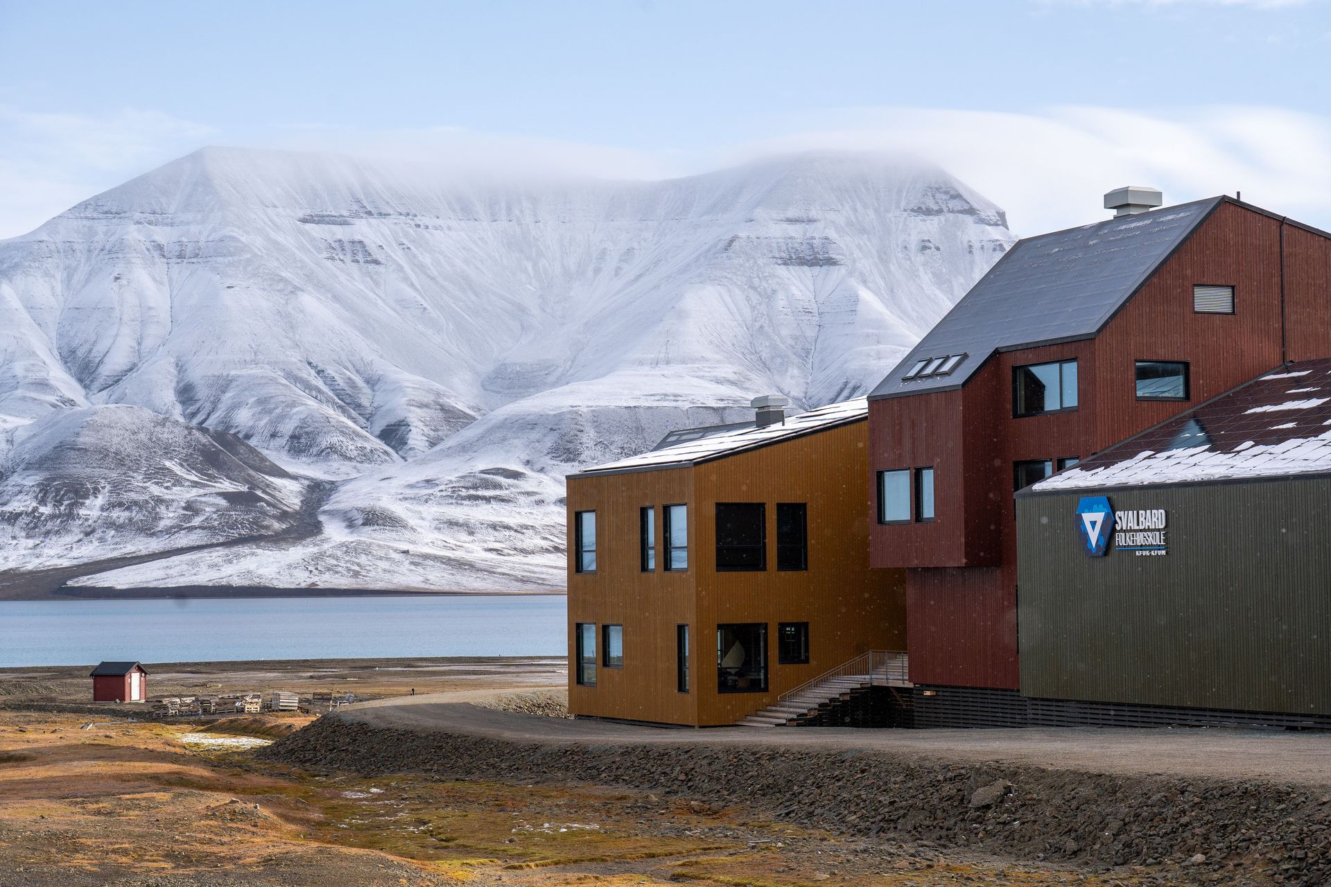 Bâtiment contemporain dans un cadre arctique avec des montagnes enneigées et une mer glacée en arrière-plan.