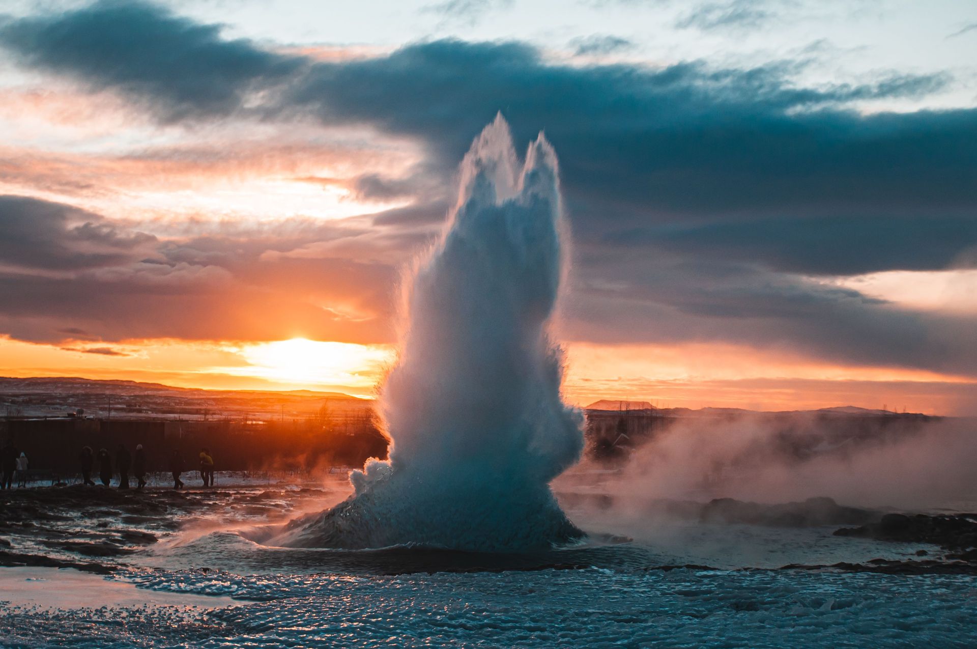 Éruption de geyser captivante avec un coucher de soleil vibrant en arrière-plan, mettant en valeur la puissance et la beauté de la nature.