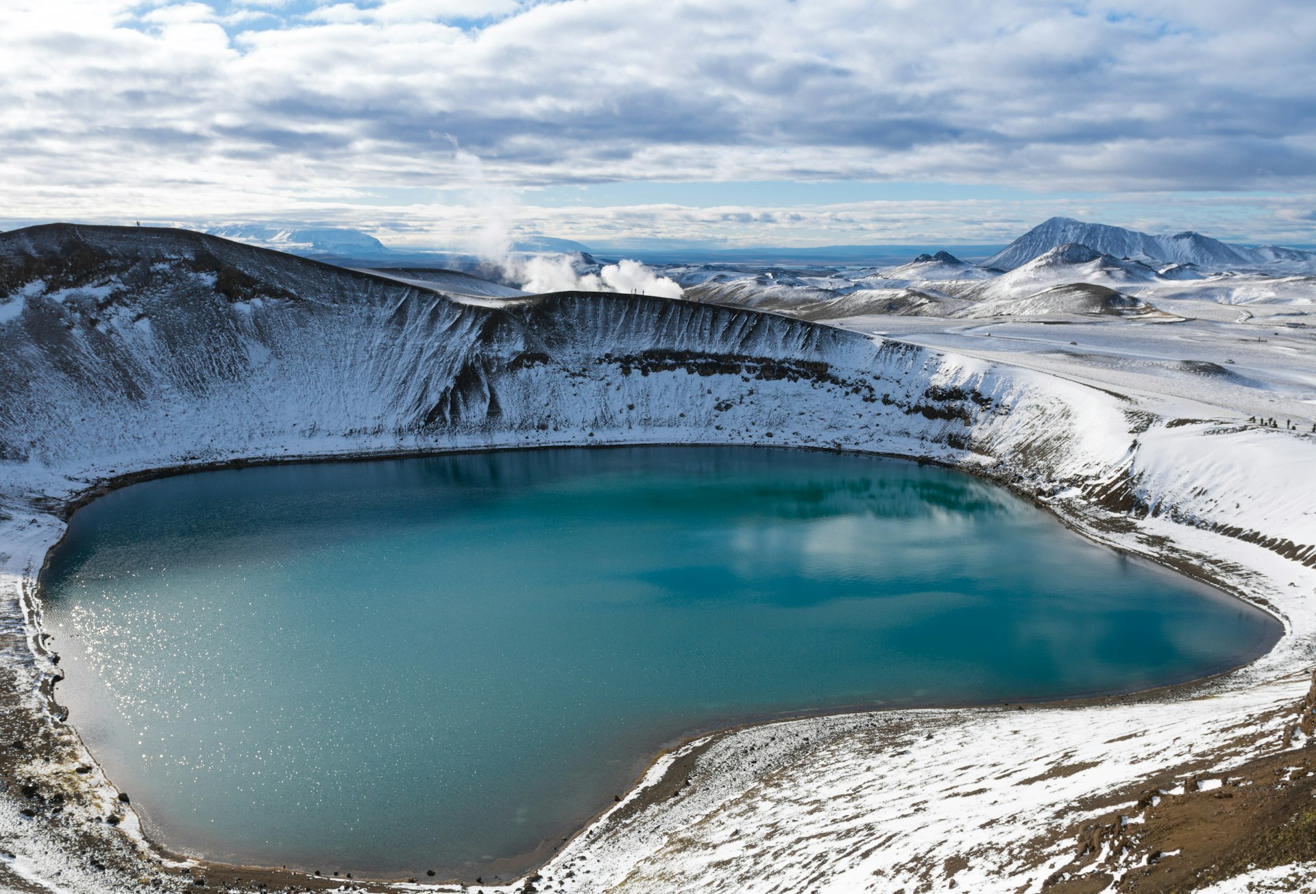 Vue à couper le souffle d'un lac de cratère volcanique en Islande, entouré de terrains enneigé.