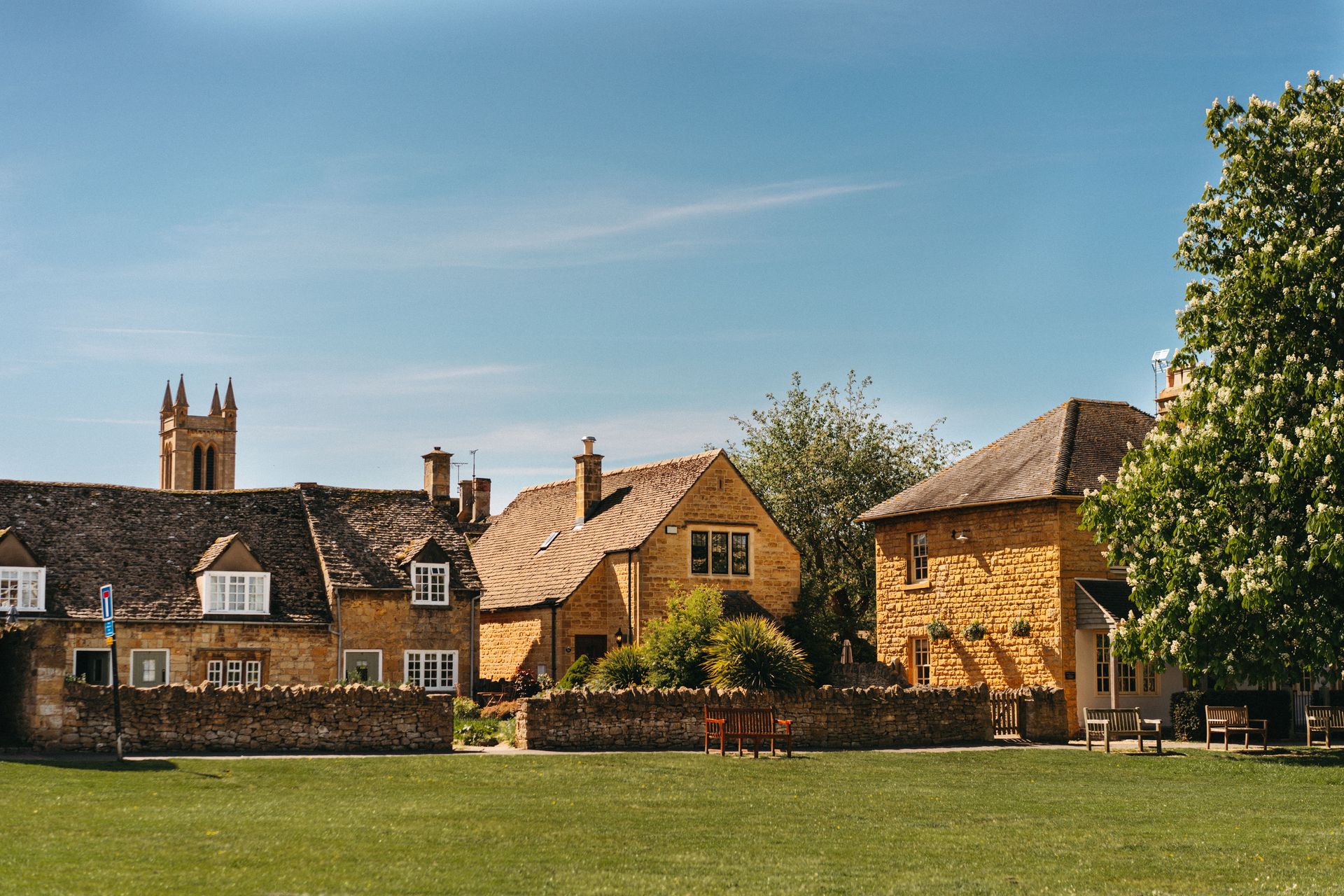 Une vue pittoresque des maisons traditionnelles en pierre des Cotswolds sous un ciel bleu limpide.  Plus d’infos  Partager