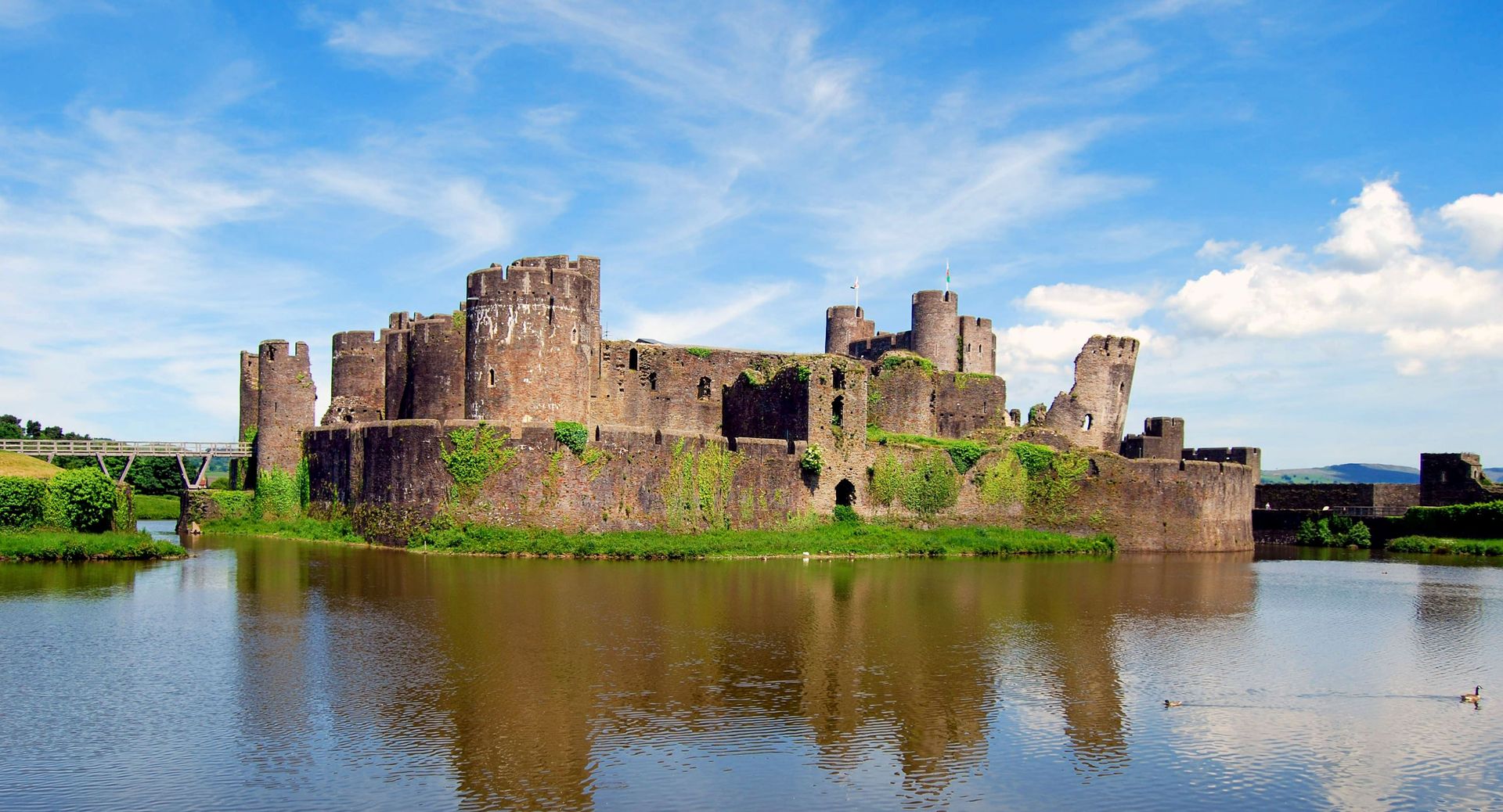 Explorez le château historique de Caerphilly qui se reflète dans les eaux sereines sous un ciel bleu azur.