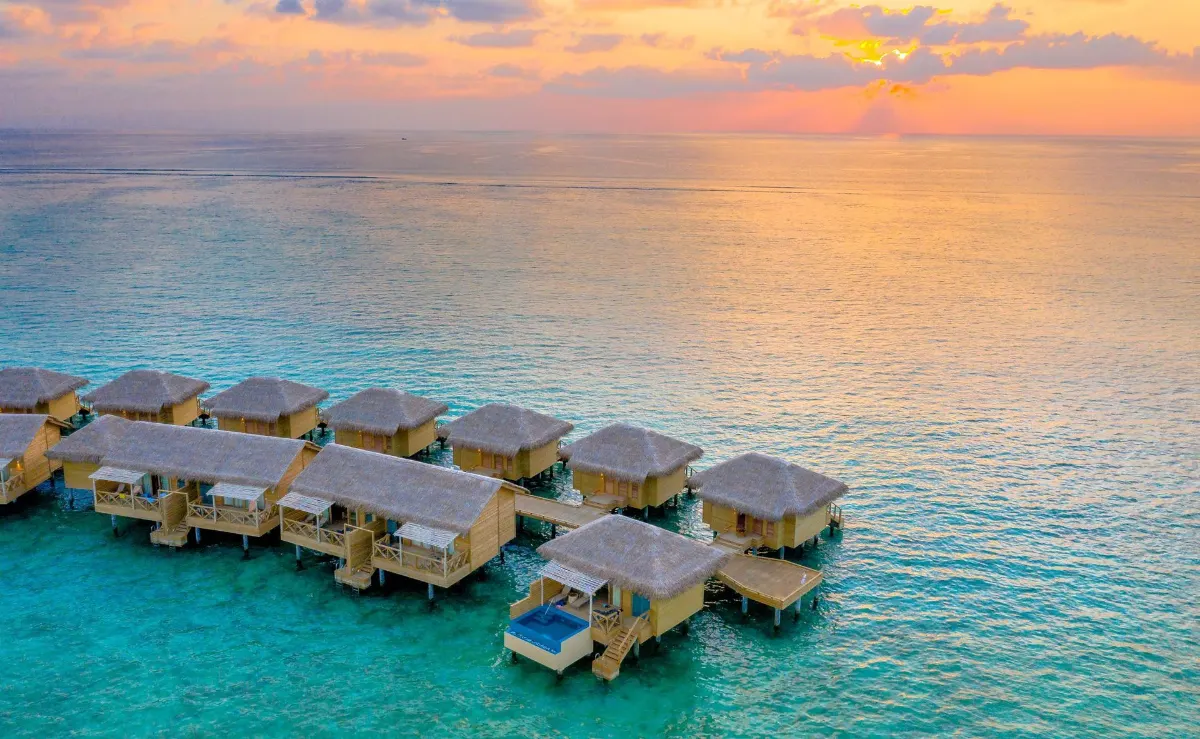 Vue aérienne de magnifiques villas sur l'eau avec un coucher de soleil vibrant sur un océan tropical.