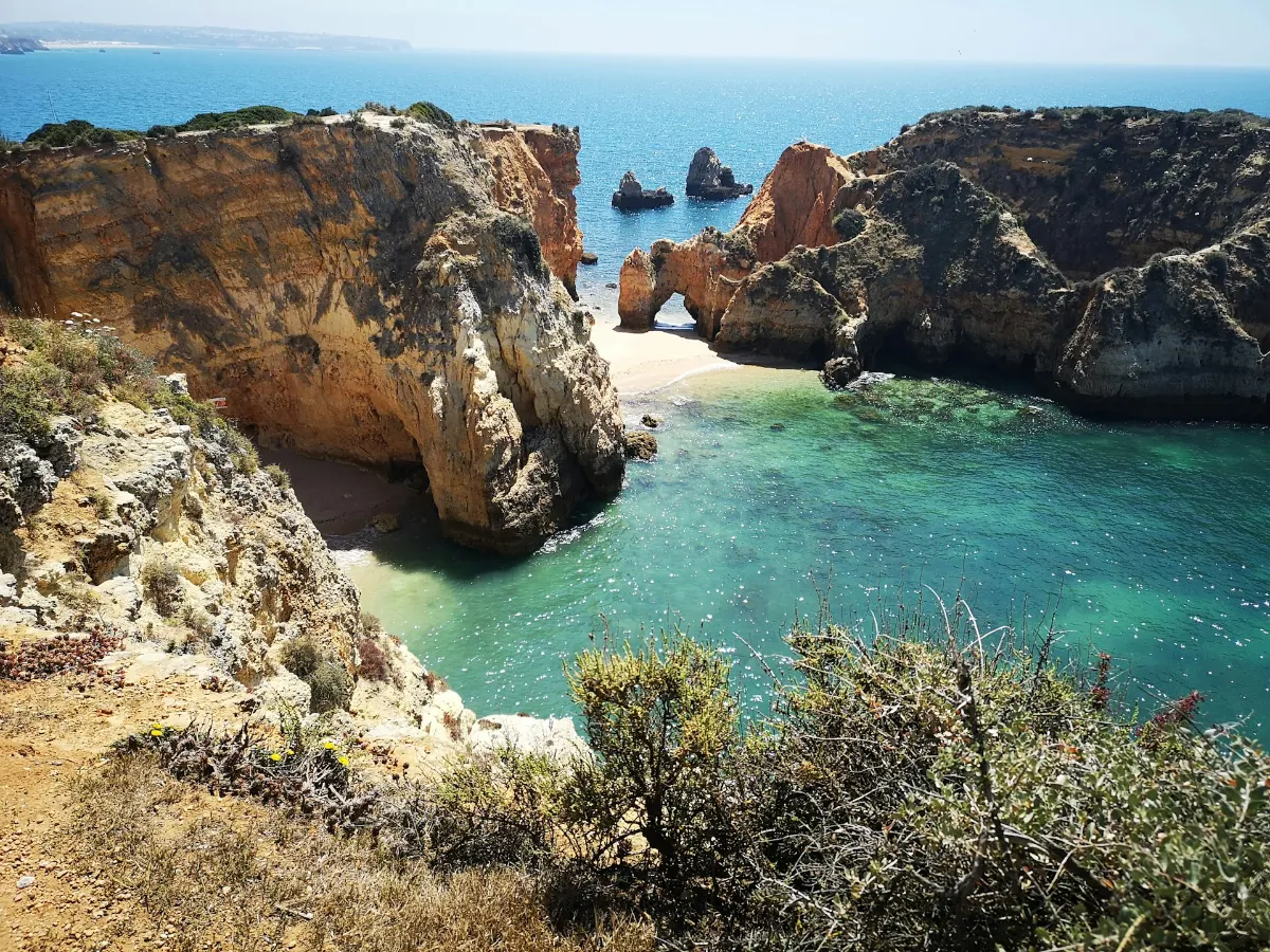 Crique cachée entre falaises ocre de l'Algarve, eau turquoise et arche rocheuse en arrière-plan, à Ponta da Piedade.