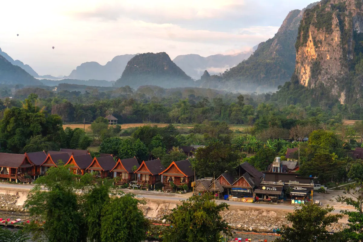 Vue de paysage apaisante de Vang Vieng, Laos, mettant en valeur des huttes, des montagnes et un paysage brumeux.