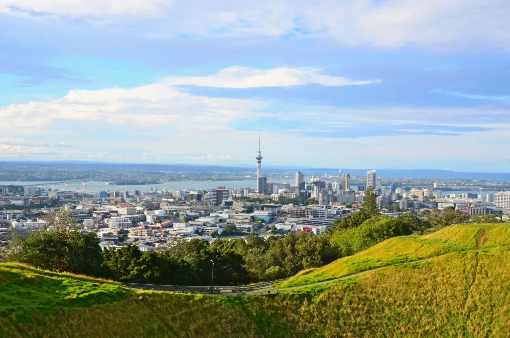 Vue imprenable sur le paysage urbain d'Auckland avec la Sky Tower et les collines luxuriantes sous un ciel clair.