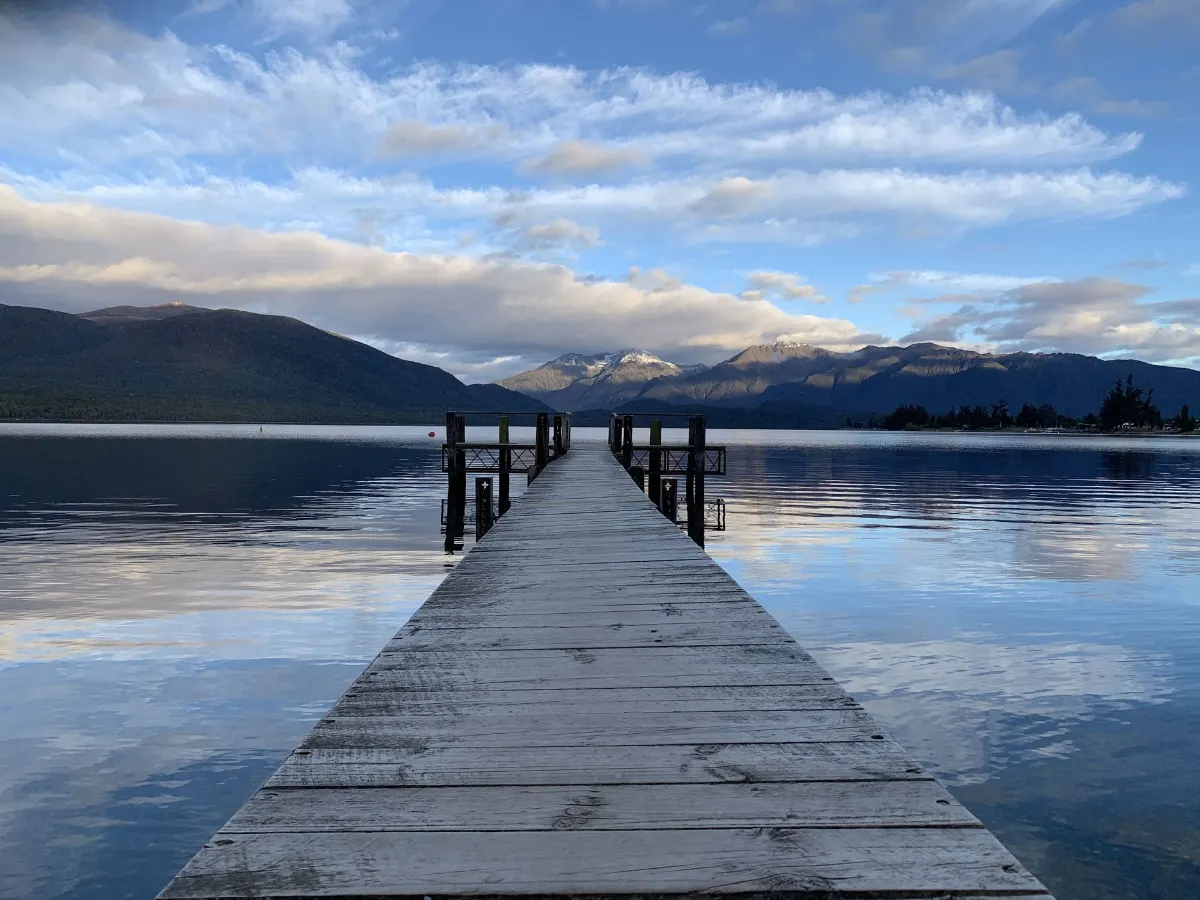 Promenade paisible menant à un lac serein dans le Southland, avec un arrière-plan montagneux.