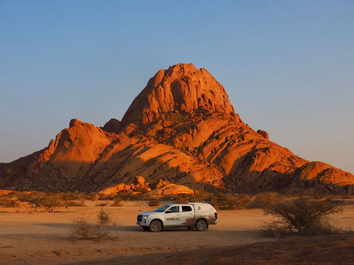 Coucher de soleil spectaculaire sur Spitzkoppe dans la région de Damaraland, en Namibie, avec une voiture au premier plan.