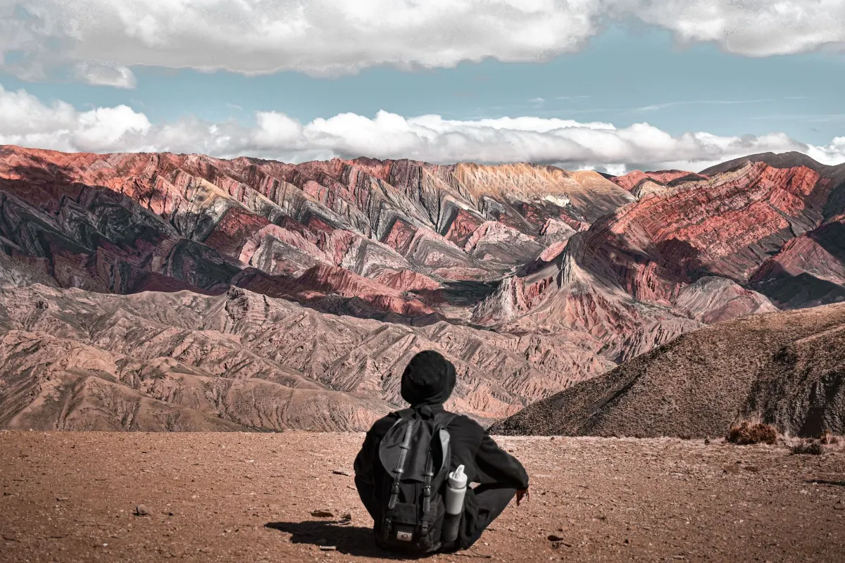 Une personne assise avec un sac à dos apprécie la vue des montagnes colorées de la Serranía de Hornocal à Jujuy, Argentine.