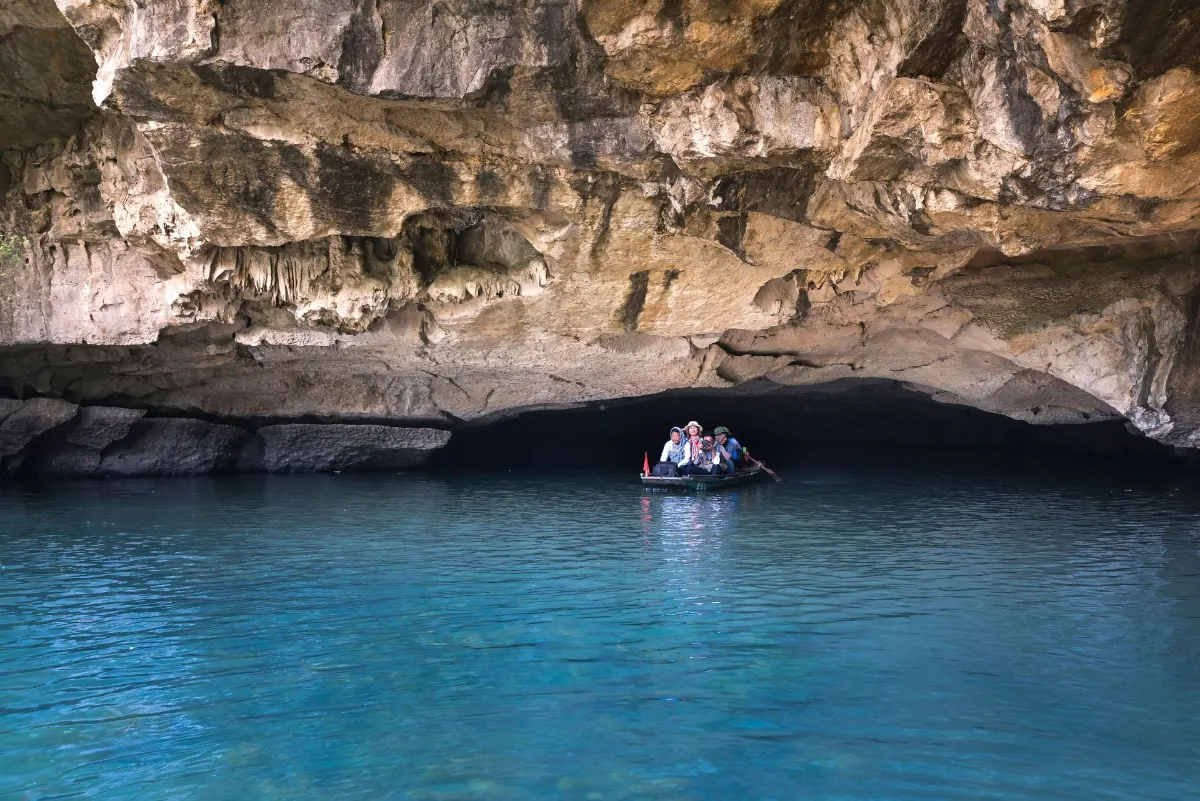 Un groupe de personnes sur un bateau explorant une grotte de calcaire pittoresque avec des eaux bleu clair.