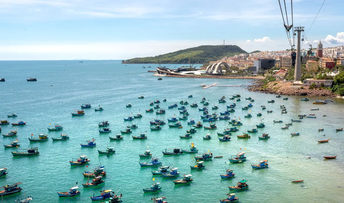 Vue aérienne de bateaux de pêche colorés sur une côte vibrante avec téléphérique et paysage urbain au Vietnam.