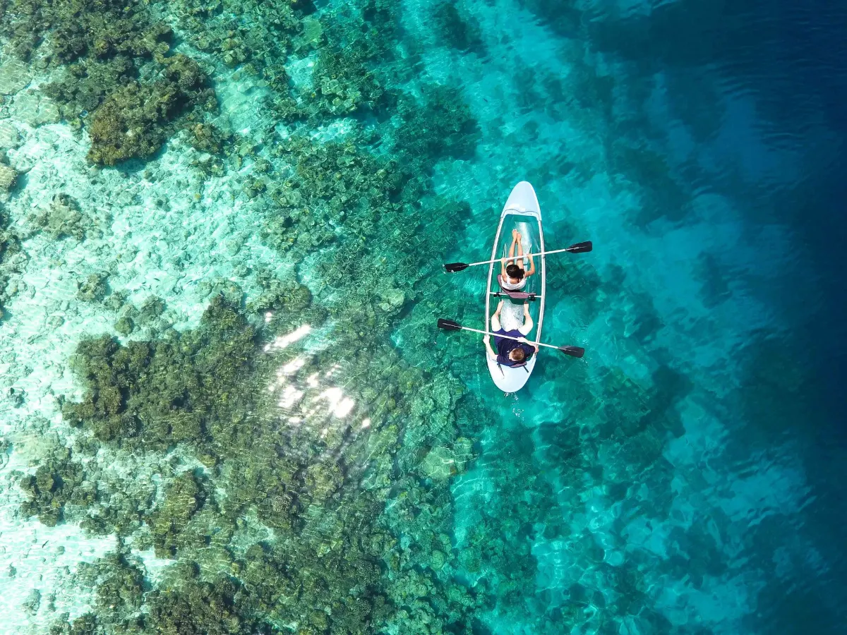 Vue aérienne d'un canoë transparent glissant sur des récifs coralliens vibrants dans les eaux turquoise des Maldives.